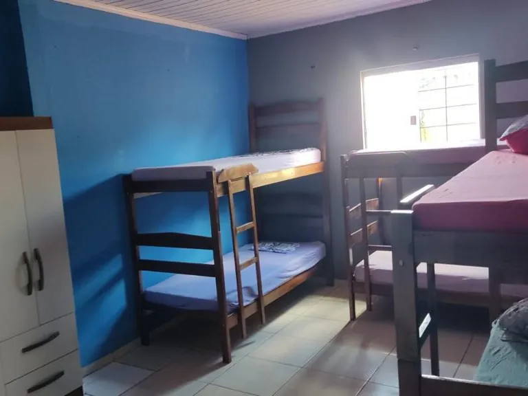 Quarto com parede azul, dois beliches de madeira, armário branco e janela clara