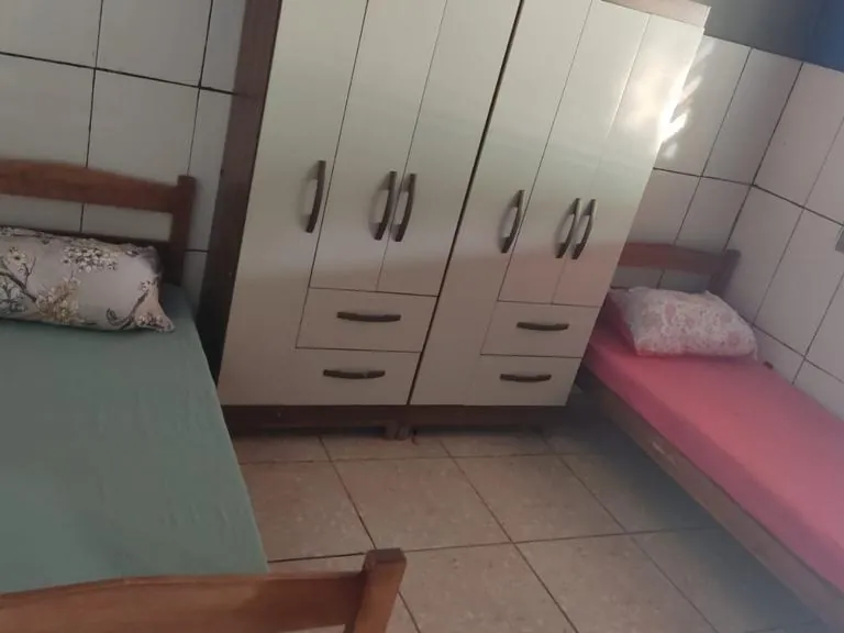 Quarto azulejado com duas camas de solteiro, lençóis verde e rosa e armário branco grande